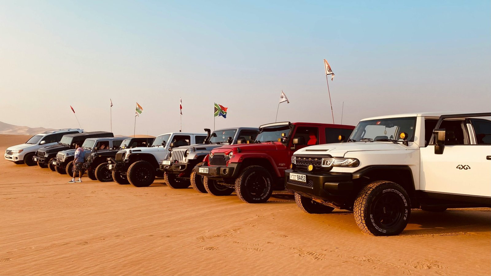 A lineup of 4x4 vehicles parked on the sandy terrain of Abu Dhabi desert with flags waving.