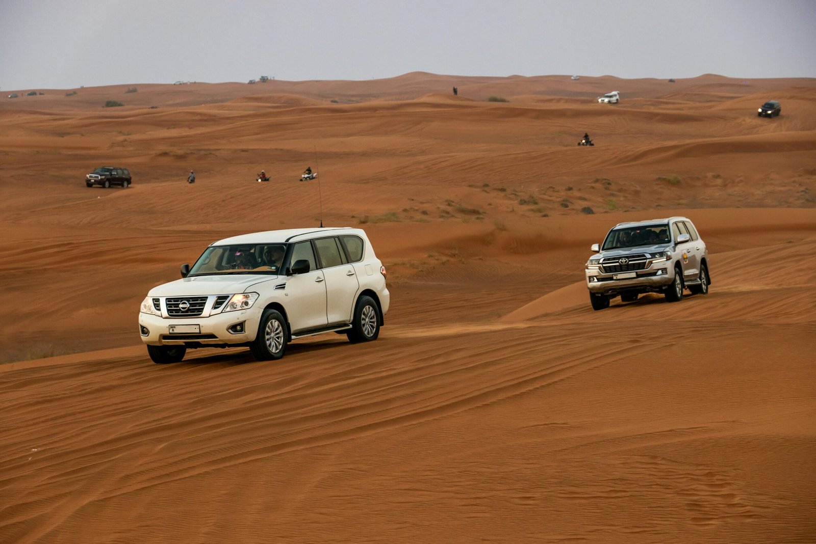 White 4x4 vehicles driving across sandy desert dunes during a thrilling safari adventure.
